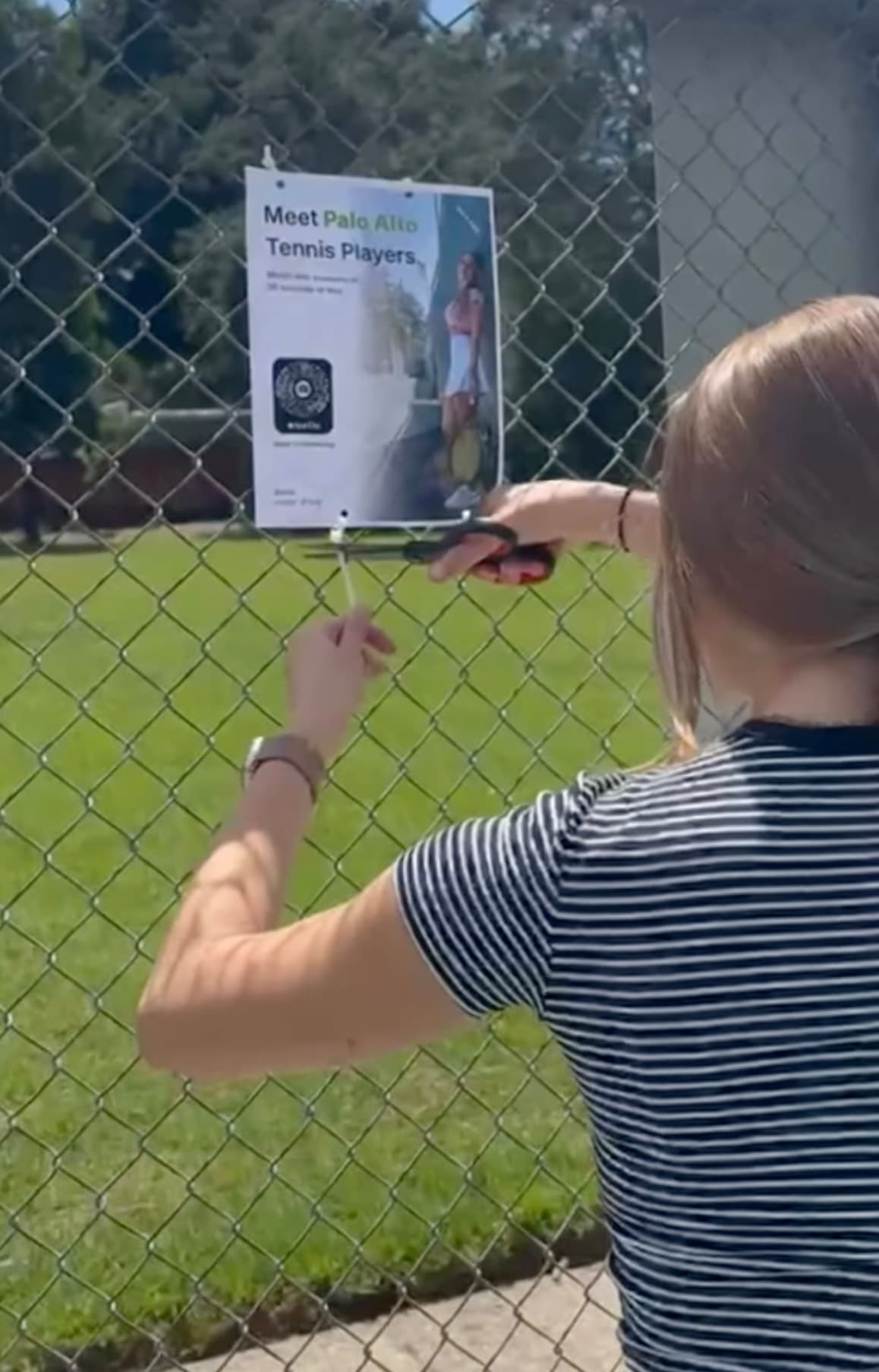 A Rally ambassador placing a flyer on a tennis court fence.